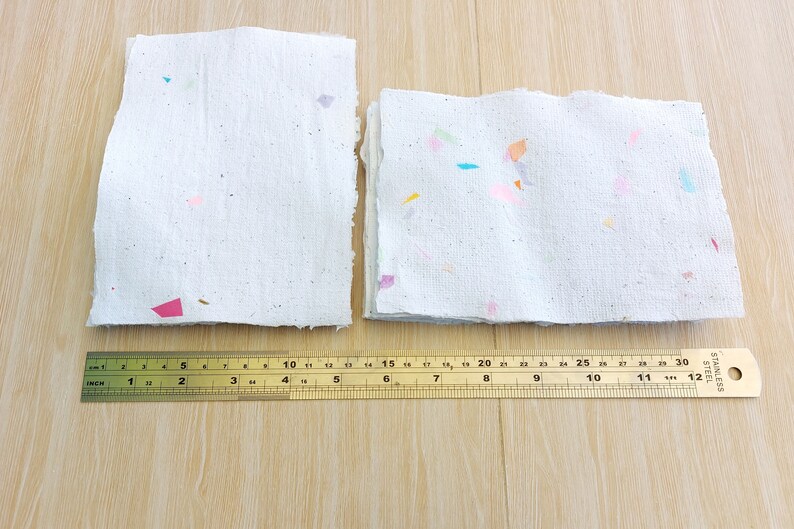 May include: Two stacks of handmade paper with colorful flecks. The paper is white and has a rough texture. A ruler is placed below the paper, measuring 12 inches.