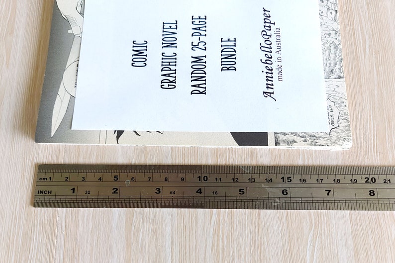Puede incluir: Un primer plano de una regla que mide una pila de libros de bolsillo. Los libros de bolsillo est&aacute;n etiquetados como "Comic", "Graphic Novel", "Random 25-Page Bundle" y "AnniebelloPaper made in Australia".