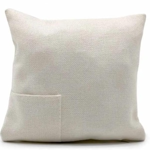 May include: A white throw pillow with a small pocket on the front. The pillow is made of a textured fabric.