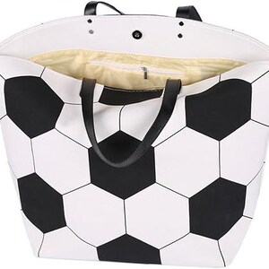 Puede incluir: Bolso tote blanco con un dise&ntilde;o de bal&oacute;n de f&uacute;tbol en blanco y negro. El bolso tiene asas negras y un bolsillo interior con cremallera. El forro interior es de color amarillo claro.