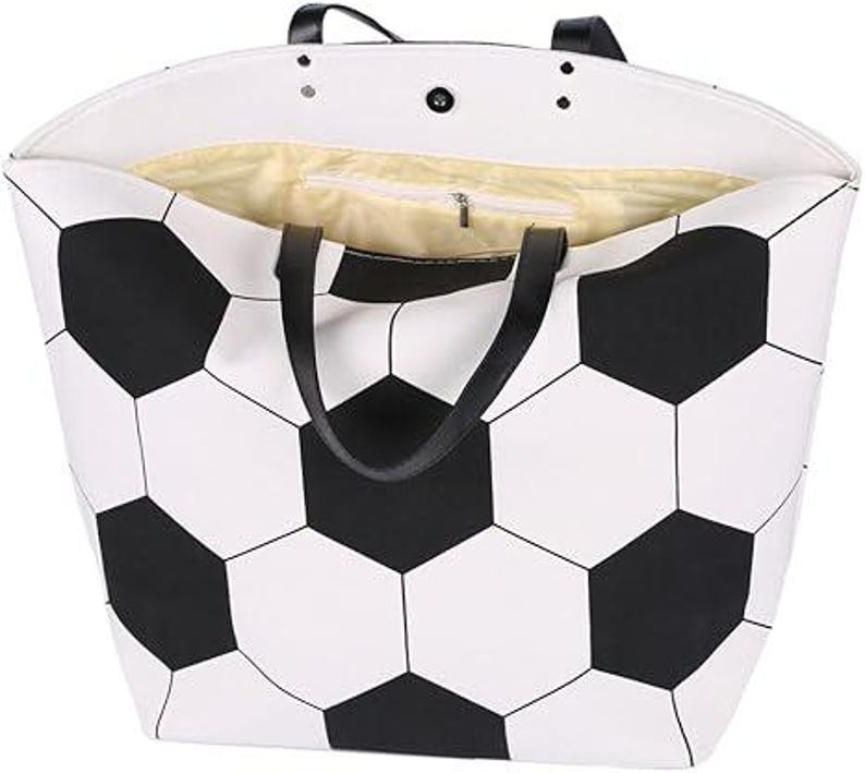 Puede incluir: Bolso tote blanco con un dise&ntilde;o de bal&oacute;n de f&uacute;tbol en blanco y negro. El bolso tiene asas negras y un bolsillo interior con cremallera. El forro interior es de color amarillo claro.