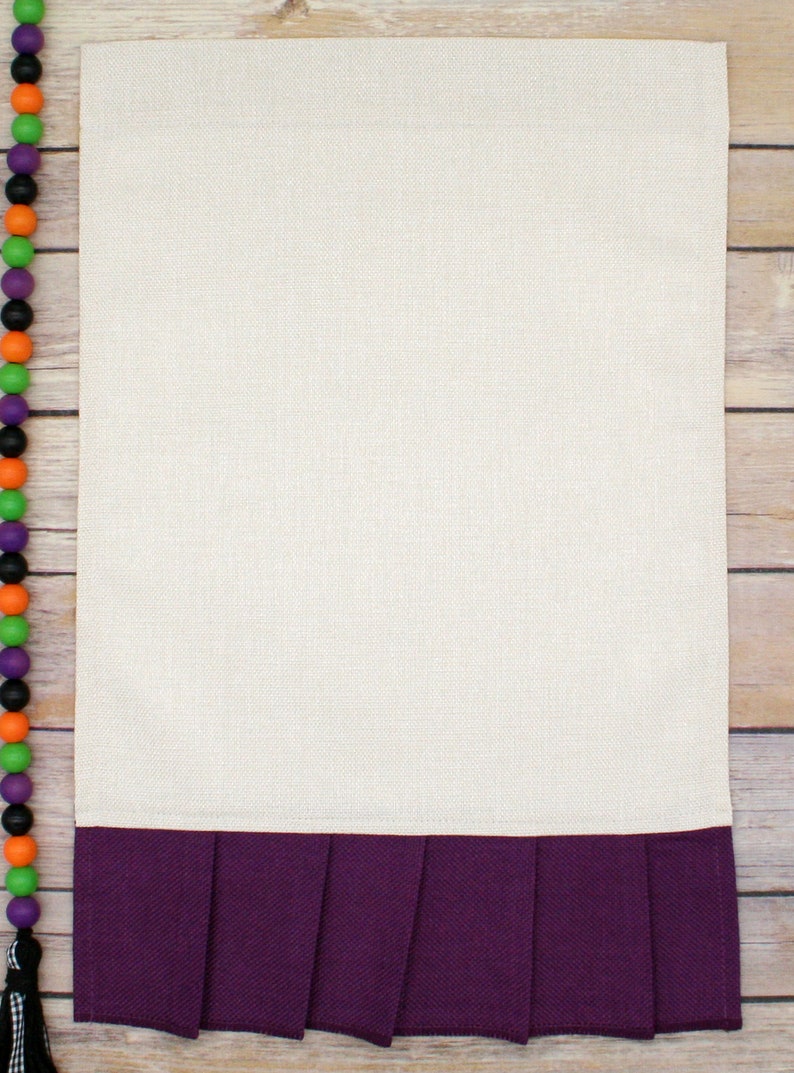 May include: A white kitchen towel with a purple ruffled bottom. The towel is on a wooden surface.
