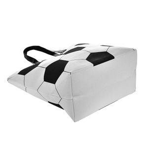 Puede incluir: Un bolso tote blanco con un dise&ntilde;o de bal&oacute;n de f&uacute;tbol en blanco y negro. El bolso tiene forma rectangular y un asa negra. El dise&ntilde;o de bal&oacute;n de f&uacute;tbol cubre la parte superior y los lados del bolso.