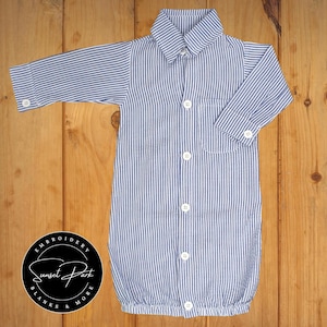 May include: A blue and white striped baby gown with a button-up front and long sleeves. The gown has a small pocket on the left side.