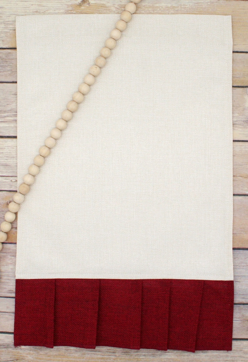 May include: A beige kitchen towel with a red ruffled bottom. The towel is decorated with a strand of wooden beads.