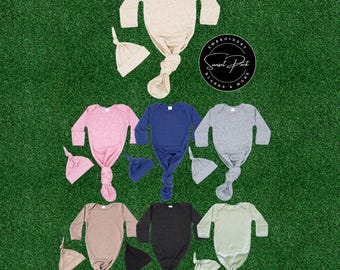 May include: A collection of baby gowns and matching knot hats in various colors, including pink, blue, gray, and beige. The gowns have long sleeves and a knotted bottom. The image is on a green background, with a logo in the upper right corner.