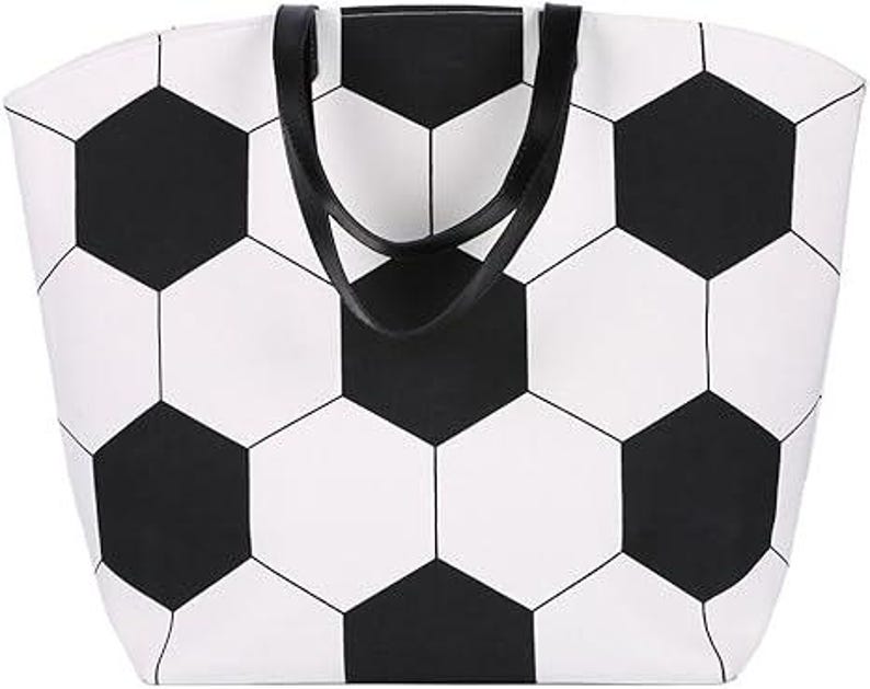 Puede incluir: Un bolso tote blanco con un dise&ntilde;o de bal&oacute;n de f&uacute;tbol negro. El bolso tiene asas negras y forma rectangular. El dise&ntilde;o del bal&oacute;n de f&uacute;tbol est&aacute; formado por formas hexagonales negras y blancas.