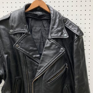 May include: Black leather motorcycle jacket with a zip fastening and multiple pockets. The jacket has a classic biker style with a stand-up collar and snap closures.