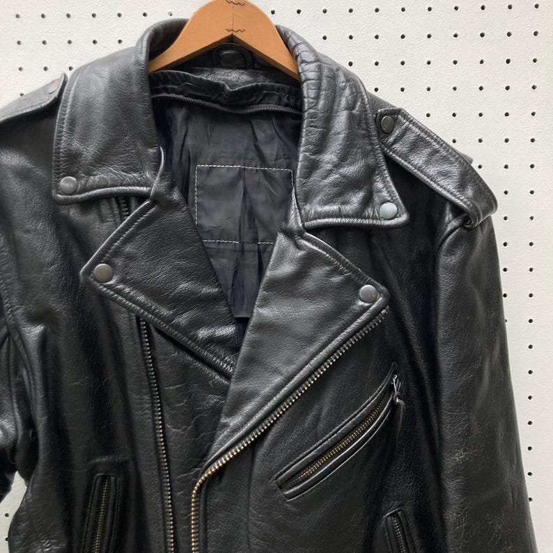 May include: Black leather motorcycle jacket with a zip fastening and multiple pockets. The jacket has a classic biker style with a stand-up collar and snap closures.