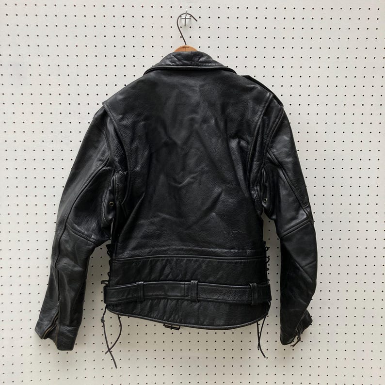 May include: Black leather motorcycle jacket with a zip fastening, a belt at the waist, and lace-up details on the sides.