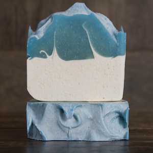 May include: Two bars of handmade soap, one on top of the other. The top bar is blue and white with a swirl design. The bottom bar is blue with a swirl design.