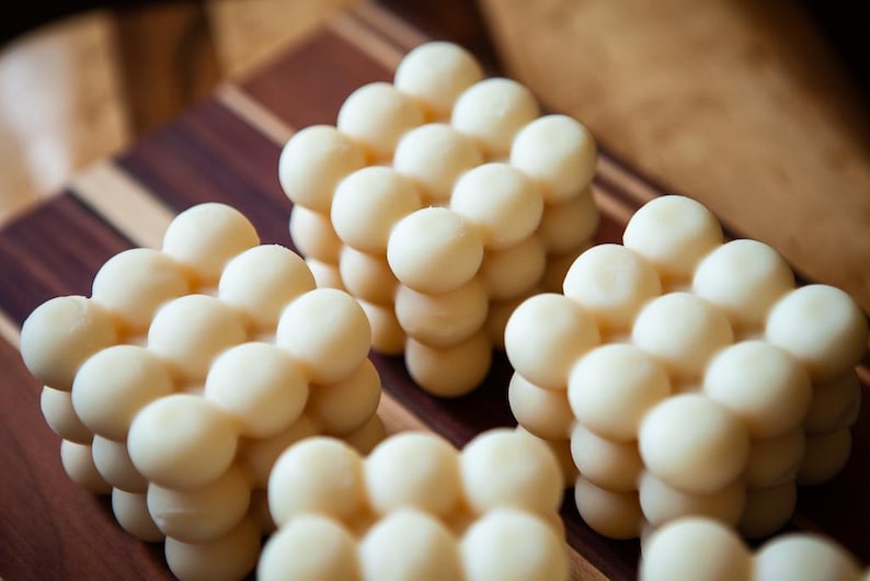 May include: Close-up of several cube-shaped arrangements of small, round, off-white objects. The objects are arranged in a grid-like pattern, creating a textured surface. The background is a wooden cutting board with dark brown and light brown stripes.