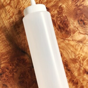 May include: A white plastic squeeze bottle with a pointed tip. The bottle is empty and has a smooth surface.