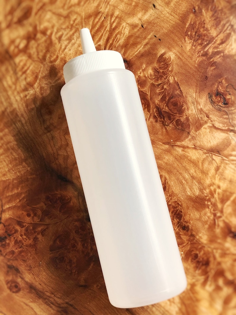May include: A white plastic squeeze bottle with a pointed tip. The bottle is empty and has a smooth surface.