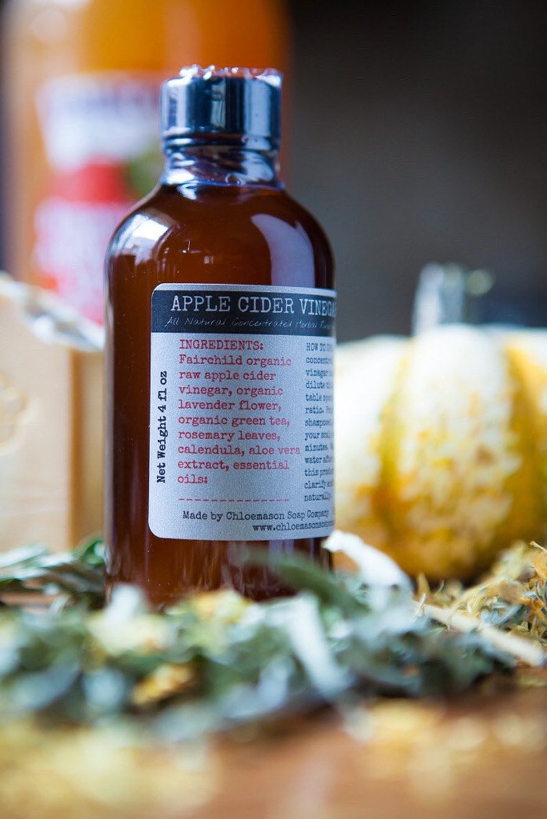 May include: A brown glass bottle with a label that reads "Apple Cider Vinegar" and lists ingredients including Fairchild organic raw apple cider vinegar, organic lavender flower, organic green tea, rosemary leaves, calendula, aloe vera extract, and essential oils. The bottle is 4 fluid ounces and is made by Chloemason Soap Company.
