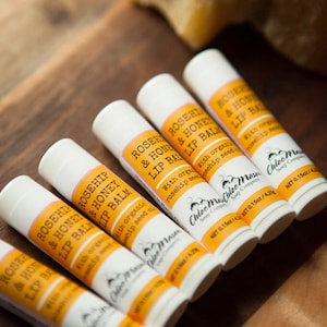 May include: Six white tubes of rosehip and honey lip balm with yellow labels. The labels have the text "Rosehip & Honey Lip Balm" and "Chloe Mae Soap Company". Each tube is labeled with a net weight of 0.15 oz / 4.2 g.