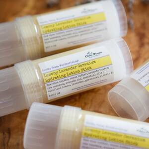May include: Three white plastic tubes with yellow labels containing a lemony lavender geranium hydrating lotion stick. The labels list the ingredients, including shea butter, cocoa butter, avocado butter, beeswax, avocado oil, essential oils, and vitamin E. The label also states "Sooth, Calm, Moisturizing!" and "Net 2 oz."