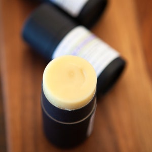 May include: A close-up of a yellow deodorant stick in a black container. The container has a label with white text.