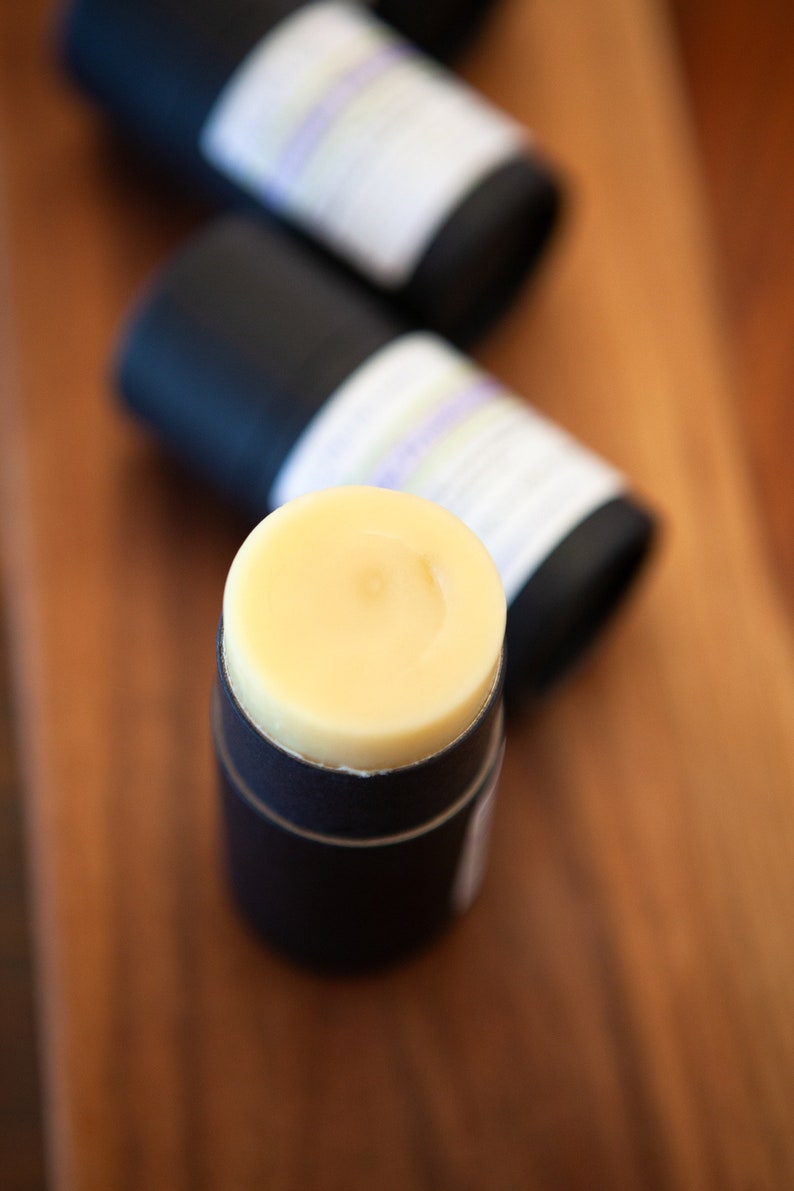 May include: A close-up of a yellow deodorant stick in a black container. The container has a label with white text.