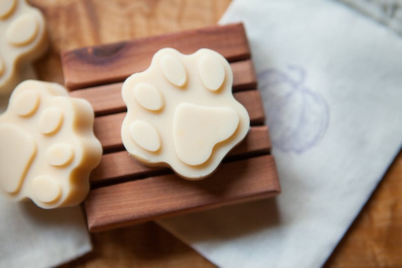 May include: Three white paw-shaped soaps on a wooden soap dish. The soaps are made with natural ingredients and are ideal for sensitive skin.