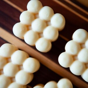 May include: Close-up of several off-white, honeycomb-shaped soaps. The soaps are arranged on a wooden surface with brown and tan stripes. The soaps have a smooth, rounded texture.