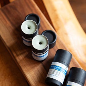 May include: Four black and green deodorant tubes with labels that read "The Patchouli Moo Pack - Grass Fed Beef Tallow & Honey Deodorant" and "Blue Patchouli Moo Pack - Grass Fed Beef Tallow & Honey Deodorant".