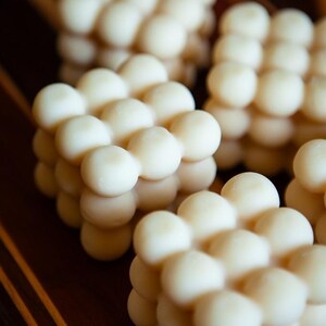 May include: Close-up of several white, spherical objects arranged in a grid-like pattern. The objects are clustered together, creating a textured, three-dimensional effect. The background is a dark, wooden surface.