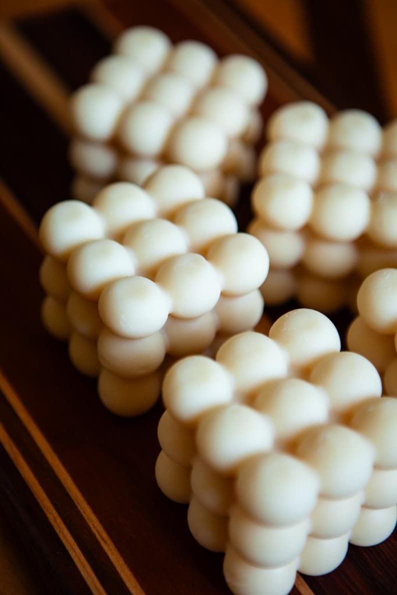 May include: Close-up of several white, spherical objects arranged in a grid-like pattern. The objects are clustered together, creating a textured, three-dimensional effect. The background is a dark, wooden surface.