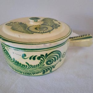 May include: A white ceramic casserole dish with a lid and a handle. The dish is decorated with green floral designs.