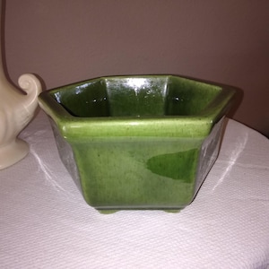May include: A green octagonal ceramic planter with a smooth, glossy finish. The planter has a wide, shallow base and four small feet.