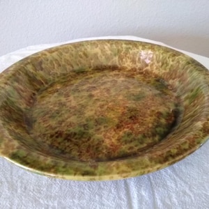 May include: Oval-shaped ceramic serving dish with a speckled pattern in shades of green, brown, and yellow. The dish has a glossy finish and a slightly raised rim. The overall aesthetic is rustic and earthy.