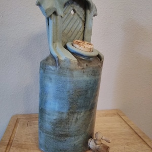 May include: A blue ceramic bottle with a wooden spout and a cork stopper. The bottle has a decorative top with a lattice design.