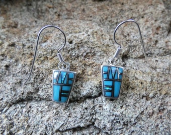 May include: A pair of silver dangle earrings with turquoise and opal inlay. The earrings are in the shape of a rectangle with a geometric design.