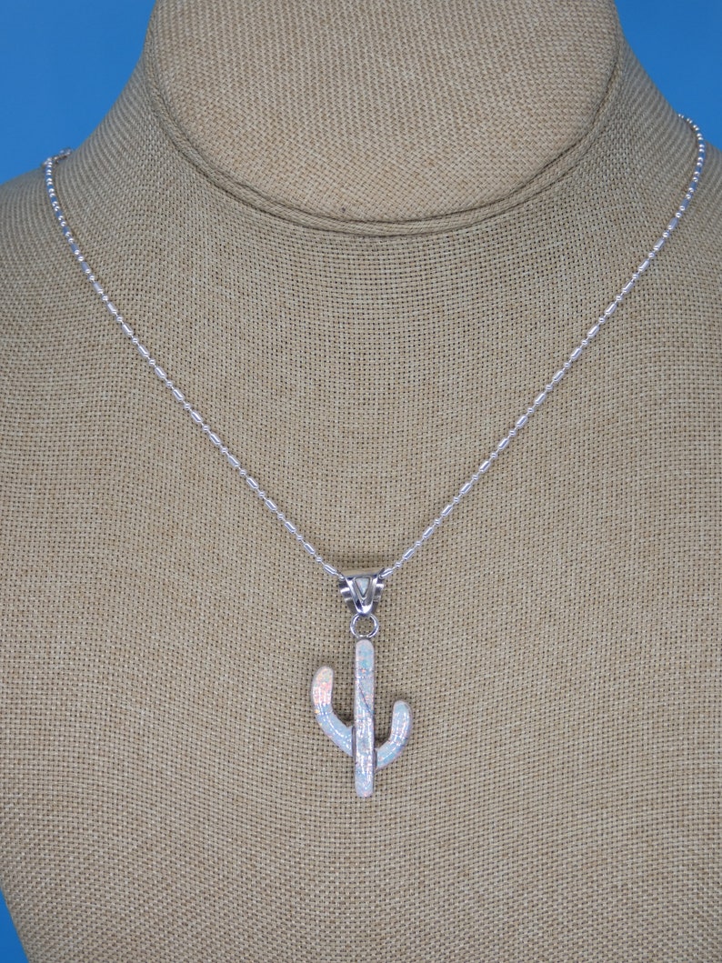 May include: A silver necklace with a cactus pendant. The pendant is white with iridescent accents, and the chain is a delicate silver. The cactus design is a stylized representation of the desert plant.