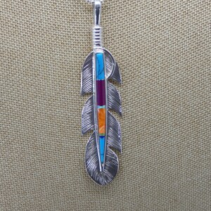 May include: A silver necklace with a feather pendant. The feather is inlaid with turquoise, red, orange, and yellow stones.