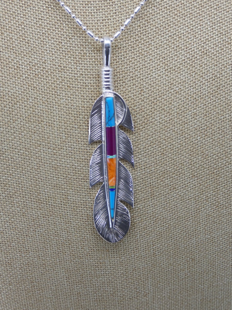 May include: A silver necklace with a feather pendant. The feather is inlaid with turquoise, red, orange, and yellow stones.