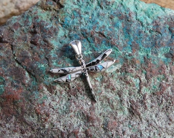 May include: A silver dragonfly pendant featuring an intricate inlay design on its wings. The wings are composed of small, geometric pieces of white shell, black stone, and iridescent blue opal, creating a mosaic effect with a polished silver body.