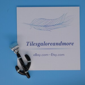 May include: A black cactus pendant with turquoise accents. The pendant is on a white card with the text "Tilesgaloreandmore" and "eBay.com~Etsy.com" printed on it. The background is a solid light blue.