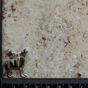 May include: A silver pendant featuring a howling wolf with inlaid turquoise, black, and brown stones. The pendant is approximately 2 inches tall.