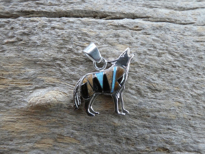 May include: A silver pendant in the shape of a howling wolf, inlaid with turquoise, black onyx, and tiger's eye stones.