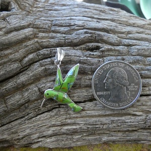 May include: A green, blue, and red enamel hummingbird pendant charm with a silver finish. The pendant is about the size of a US quarter.