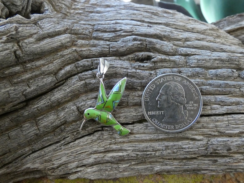 May include: A green, blue, and red enamel hummingbird pendant charm with a silver finish. The pendant is about the size of a US quarter.
