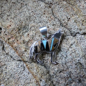 May include: A silver pendant in the shape of a howling wolf, inlaid with turquoise, black onyx, and tiger eye stones.