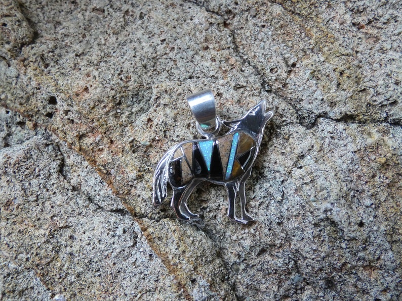 May include: A silver pendant in the shape of a howling wolf, inlaid with turquoise, black onyx, and tiger eye stones.