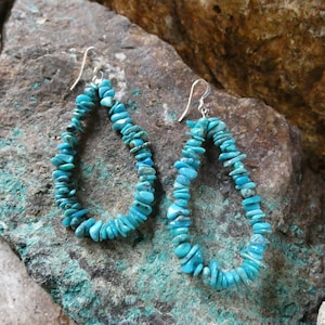 May include: A pair of turquoise teardrop earrings made with small, irregular turquoise stones. The earrings are strung on silver wire and have silver hooks.