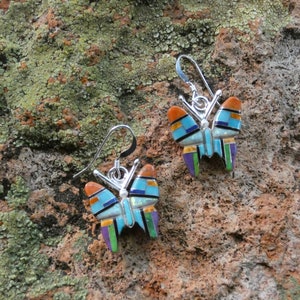 May include: A pair of silver butterfly earrings with turquoise, orange, green, purple, and black inlay.