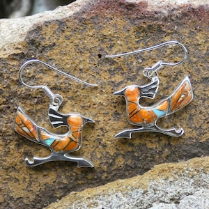 May include: A pair of sterling silver earrings featuring a roadrunner design. The earrings are inlaid with orange, brown, and turquoise stones.