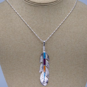 May include: A silver necklace with a turquoise, red, and orange stone feather pendant.
