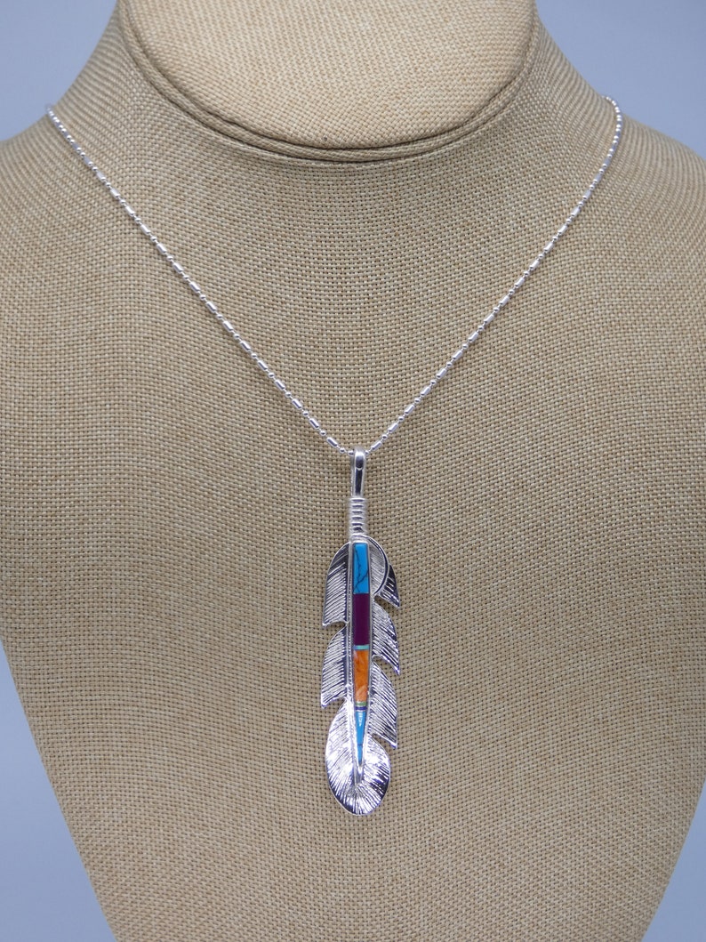 May include: A silver necklace with a turquoise, red, and orange stone feather pendant.