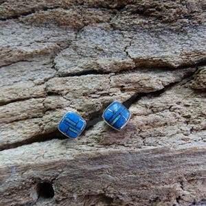May include: A pair of square stud earrings featuring a silver-toned metal frame and a mosaic inlay of vibrant blue stone segments separated by thin, dark lines. The design displays a geometric pattern with a smooth, polished surface finish.